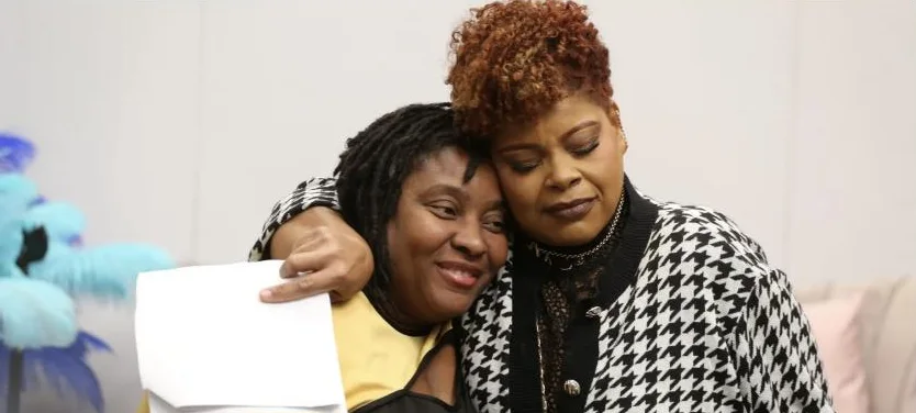 Two women share a cheek-to-cheek hug