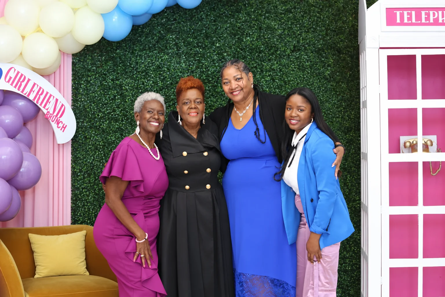 Four women of the Real Girlfriends family smile together by the balloon arch and pink phone booth